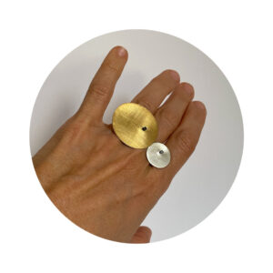 O anel Orbitas é feito com fio quadrado, banhado em ródio negro, e nele “orbitam” duas chapas circulares, uma grande com banho de ouro e outra pequena em prata fosca.