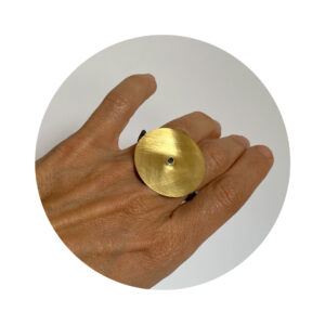 O Anel una Or é feito em fio quadrado, banhado em ródio negro, que contorna dois dedos, e sustenta chapa circular fosca, com banho de ouro 750.
