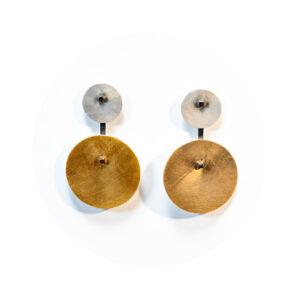 O Brinco una Orbitas tem duas chapas circulares, uma pequena em prata fosca, conectada a um pino quadrado e haste com banho de ródio, e outra grande com banho de ouro 750, que fica pendurada, conectada por esta haste.