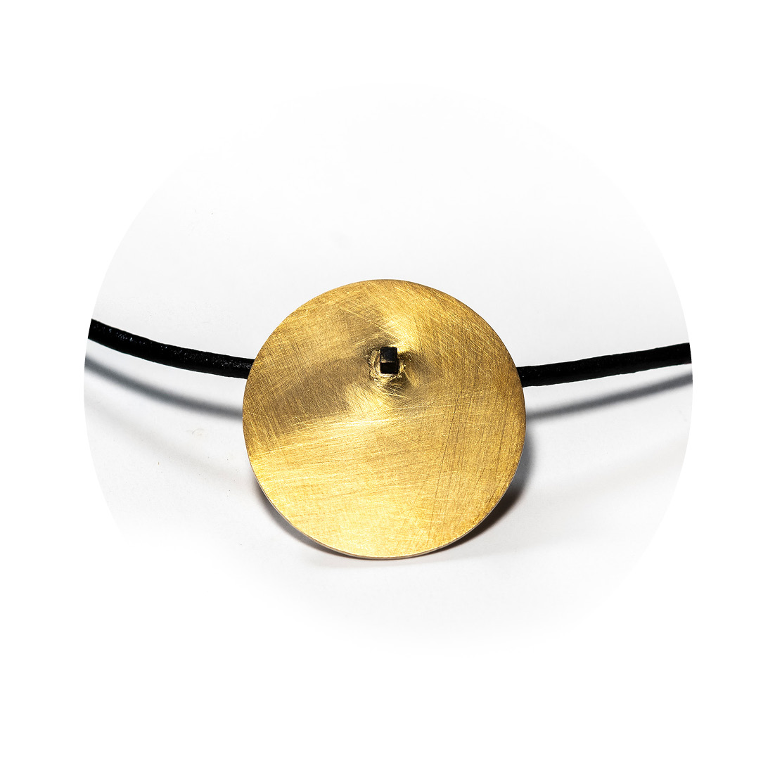 O Colar una Or é feito com fio de couro preto, com pingente em chapa circular fosca, banhada de ouro 750 e sustentada por um pino quadrado, banhado em ródio negro.