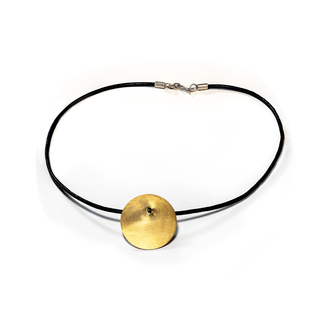 O Colar una Or é feito com fio de couro preto, com pingente em chapa circular fosca, banhada de ouro 750 e sustentada por um pino quadrado, banhado em ródio negro.